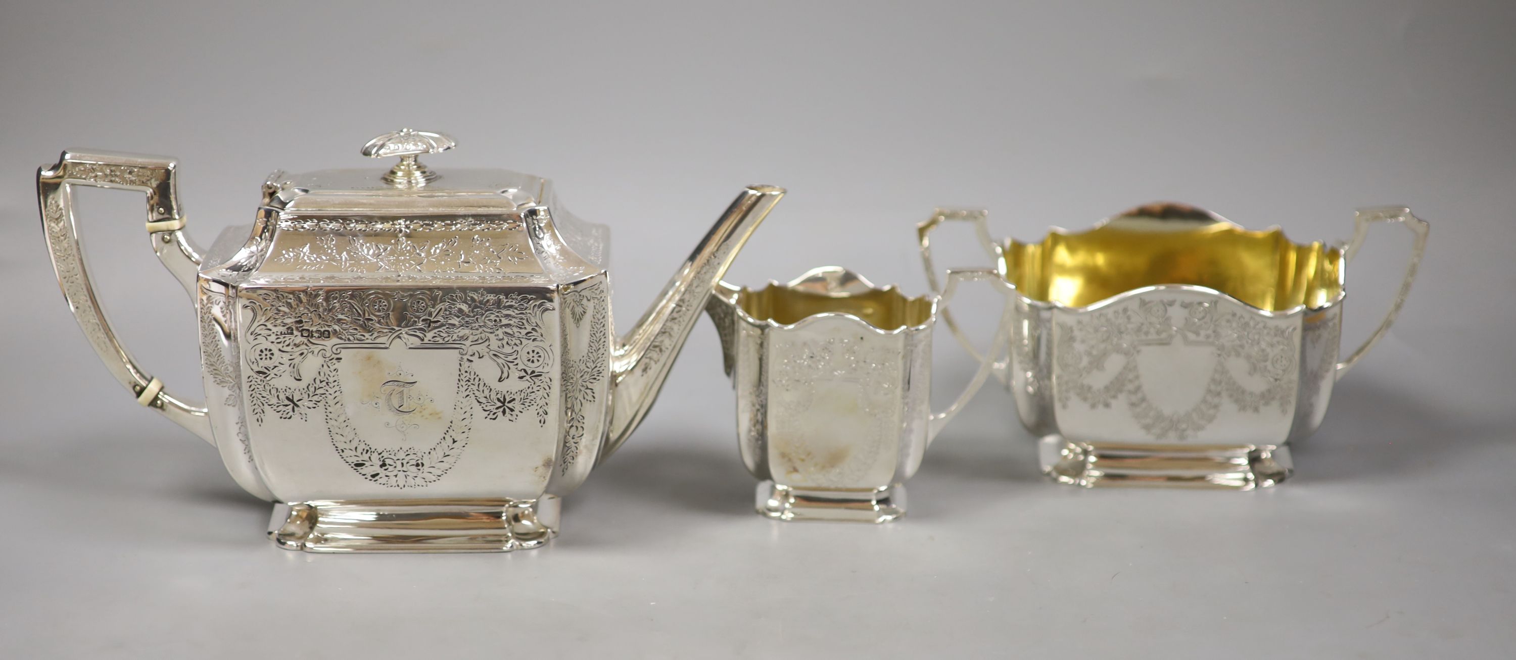 A silver three piece set, comprising teapot, twin-handled sugar basin and milk jug, with all-over chased decoration, London, 1893, by Atkins Brothers